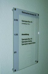 Plexitafel beschriftet mit Systemtext und mit Abstandshalter an Wand montiert